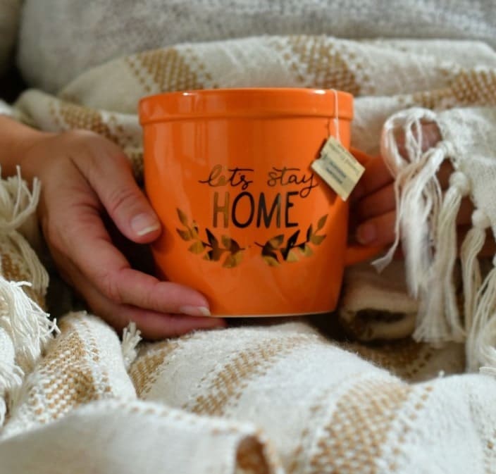 Closeup of woman holding cup in cozy blanket at home